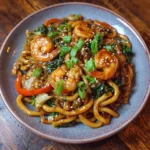 A colorful bowl of shrimp yaki udon stir-fried with vegetables and sesame seeds.